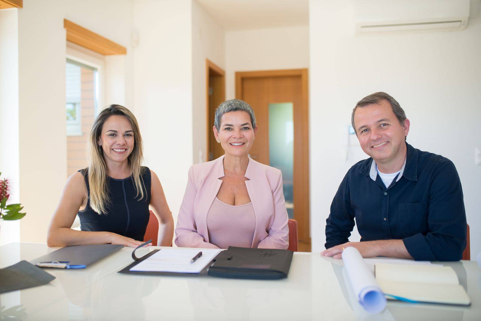 Corretora e casal sentados à mesa, assinando o contrato de locação