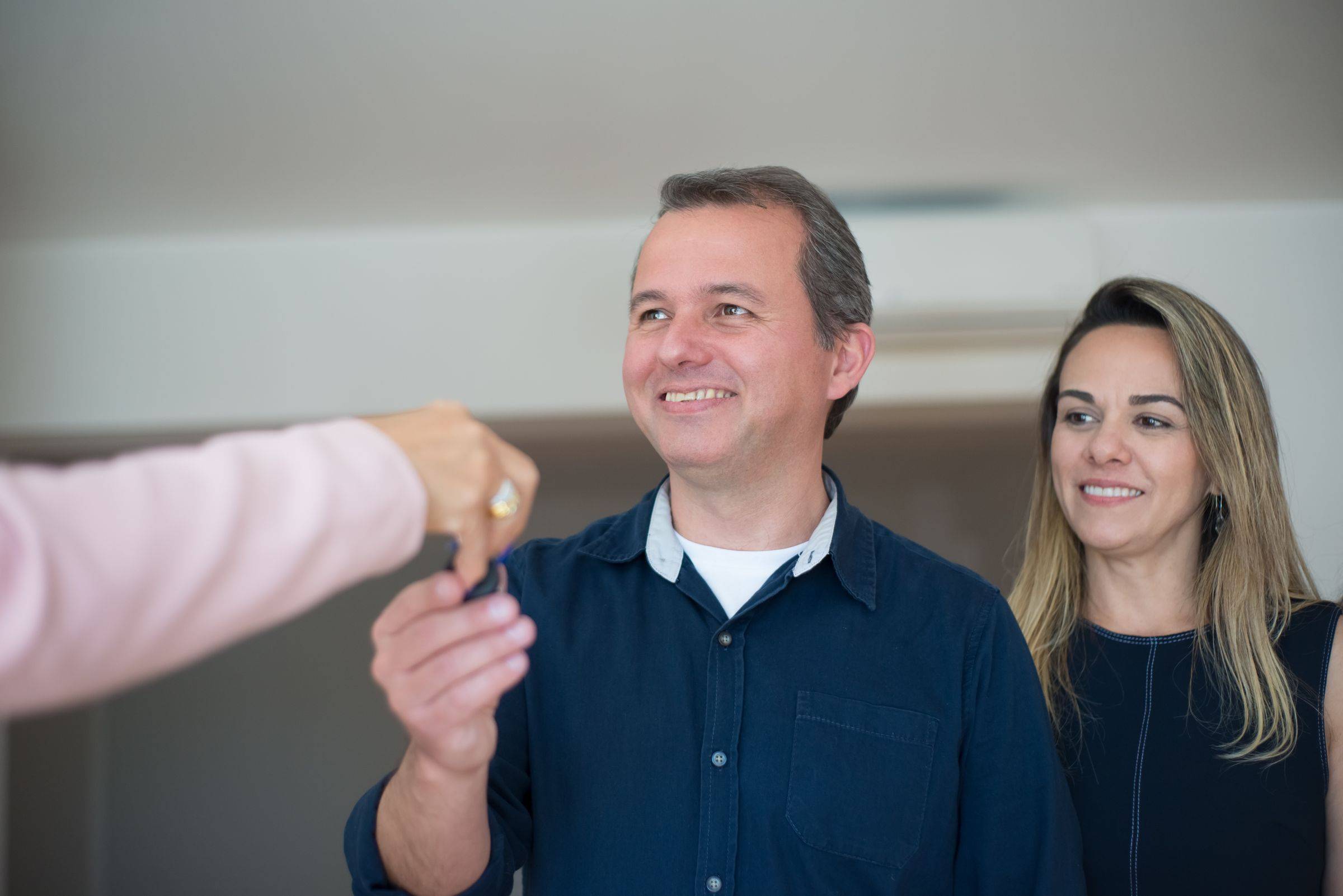 Casal sorridente recebendo a chave do novo apartamento das mãos da corretora